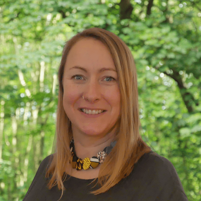 Headshot of Jinny, our CAG Somerset Lead in front of a background of leaves.